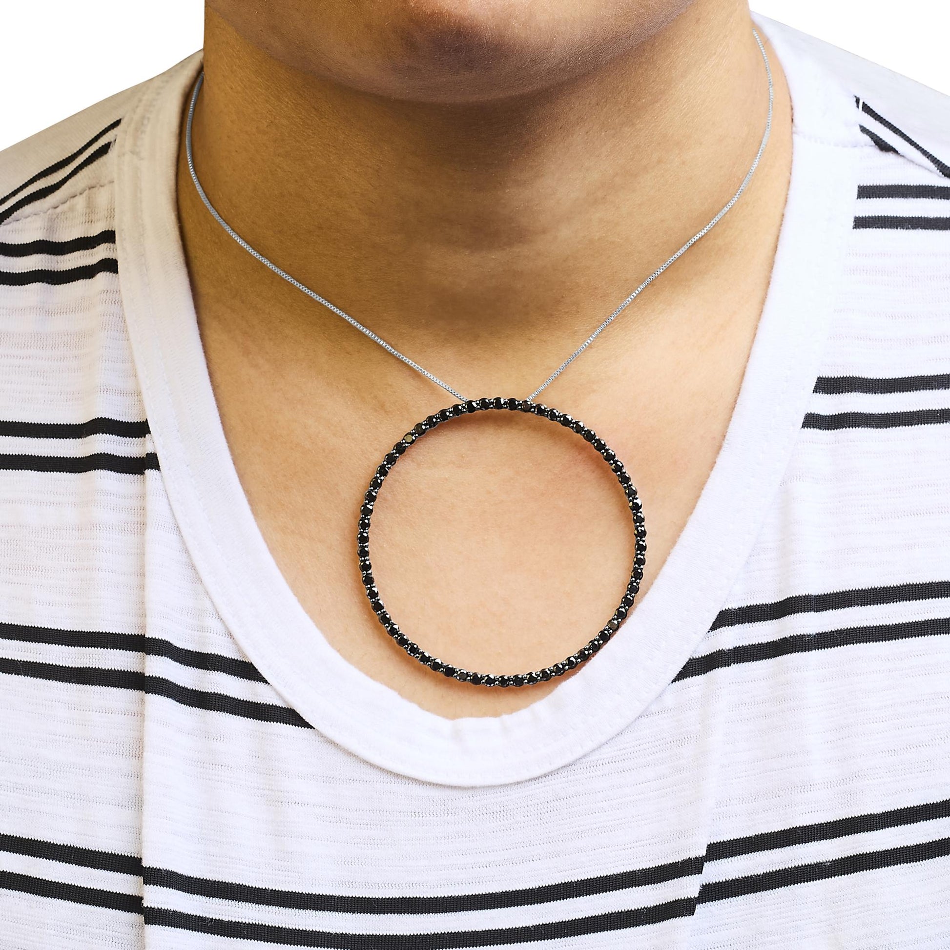 Close-up front view of a necklace on a model featuring a circular pendant with black round gemstones set in a shared prong setting on a white metal chain.