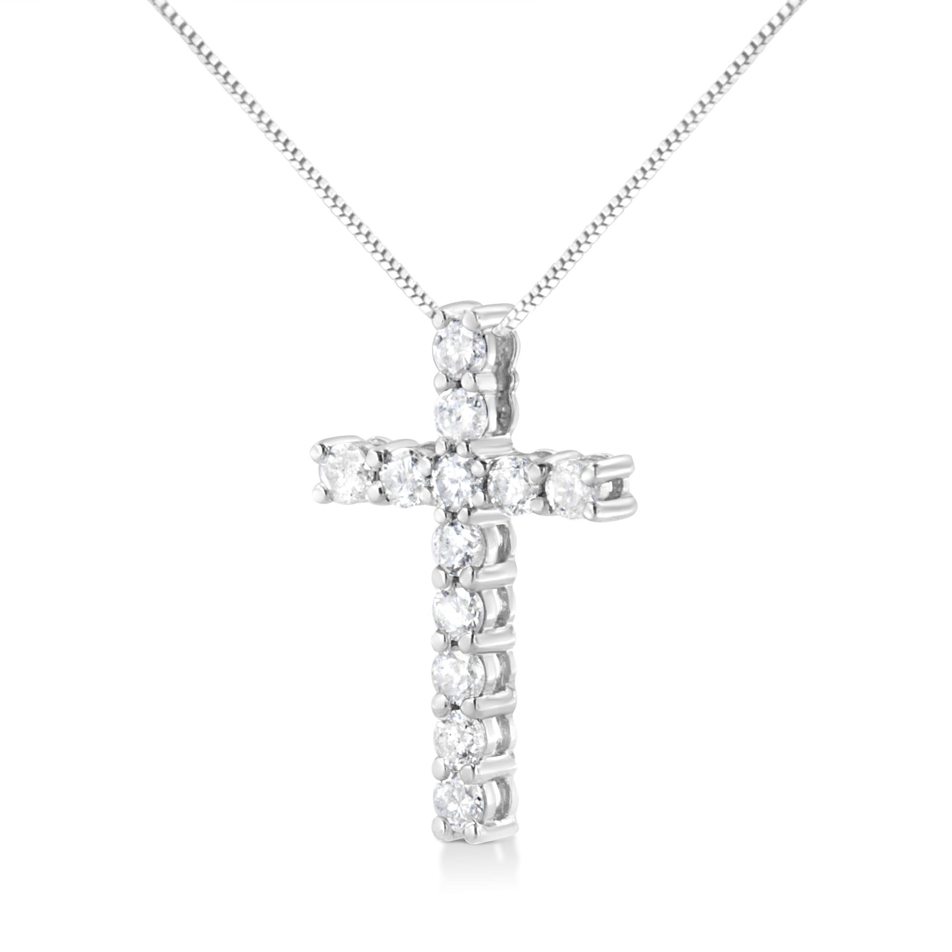 Front-facing shot of a white metal cross-shaped necklace pendant with round white gemstones in prong settings on a white metal chain.