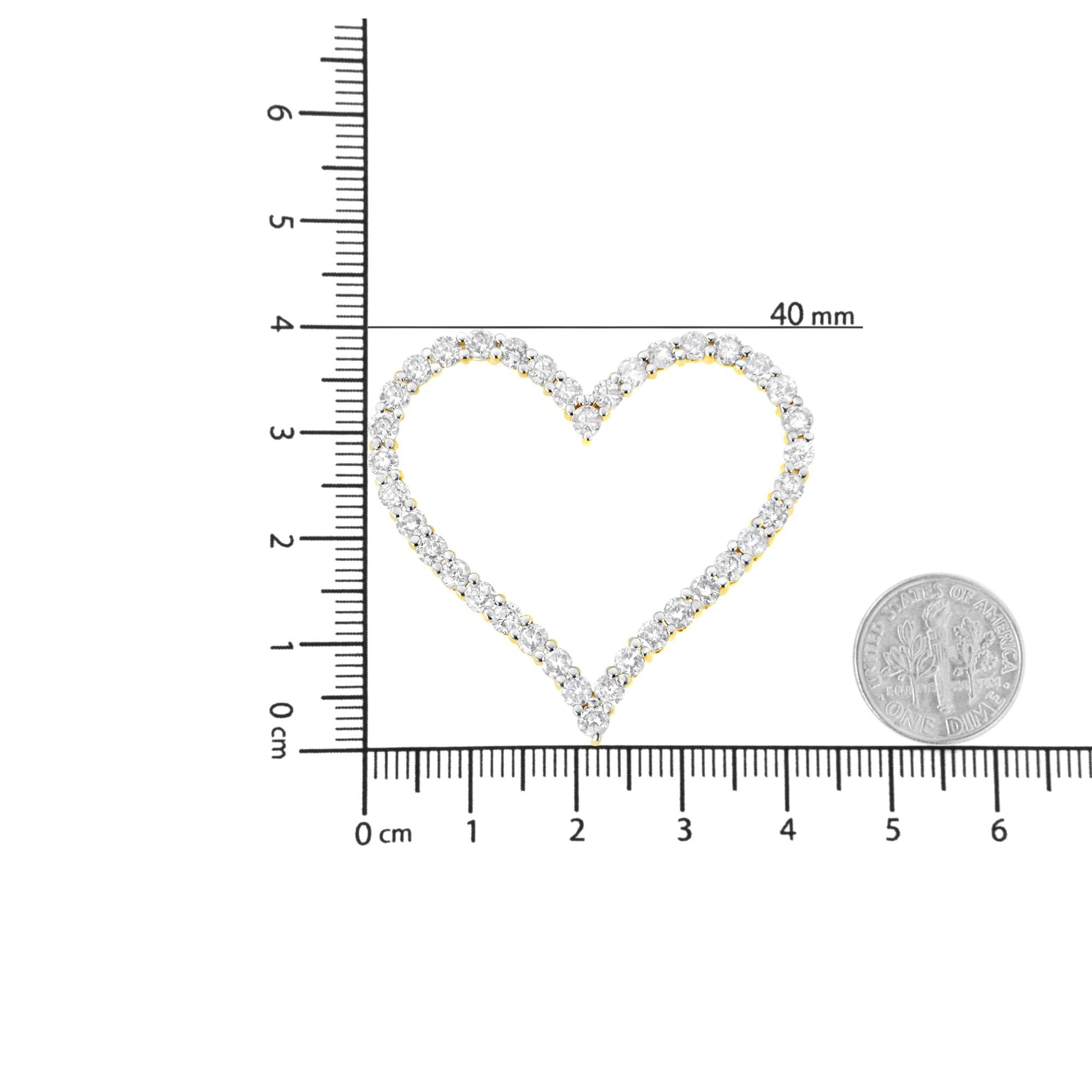 Top-down view of a yellow metal heart-shaped necklace pendant with round white gemstones in prong settings, placed on a ruler and scale for size reference next to a coin.
