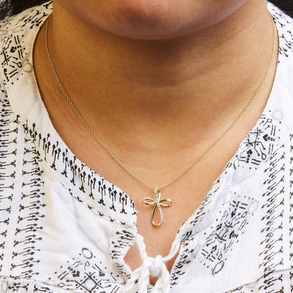 Close-up shot of a yellow metal necklace with a cross-shaped pendant featuring two white round gemstones in prong settings, worn on a model.