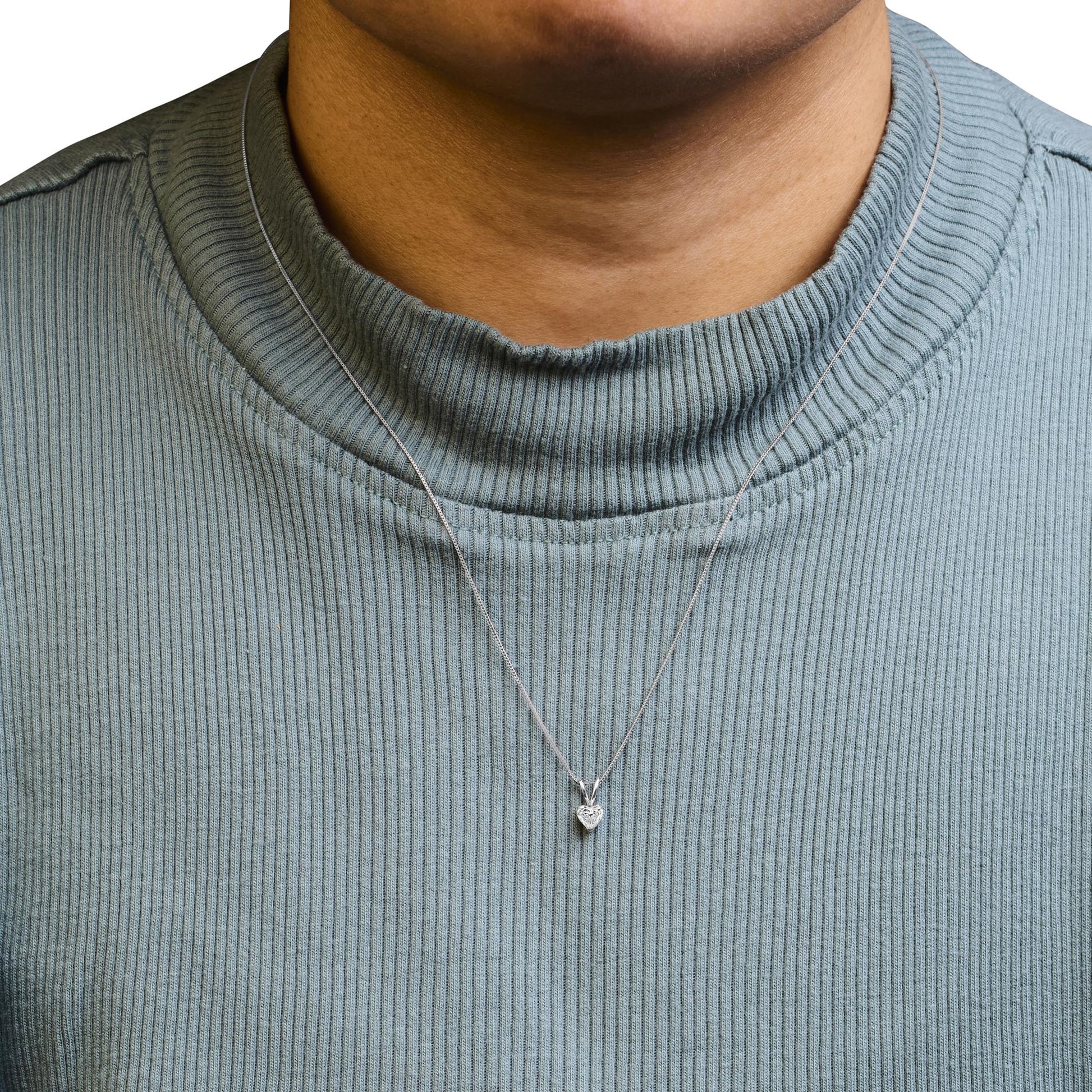 Close-up front view of a necklace on a model wearing a light blue ribbed top, featuring a white metal chain and a heart-shaped white gemstone pendant in a 3-prong setting.
