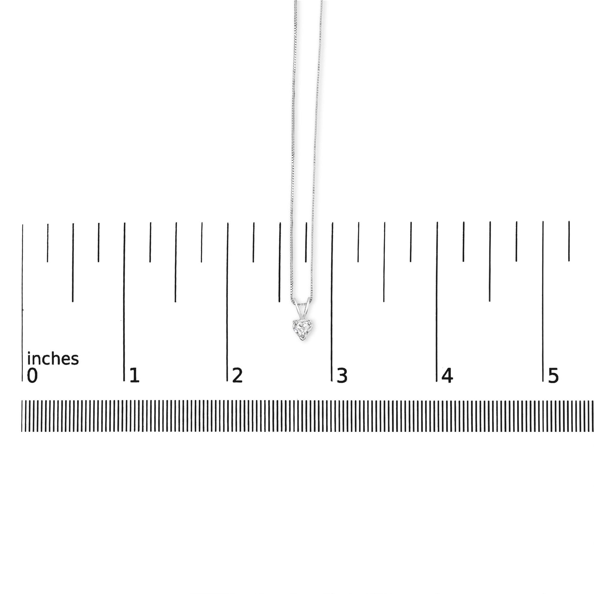 White metal necklace with a heart-shaped white gemstone pendant in a 3-prong setting, displayed hanging above a ruler for size reference, shot from the front.
