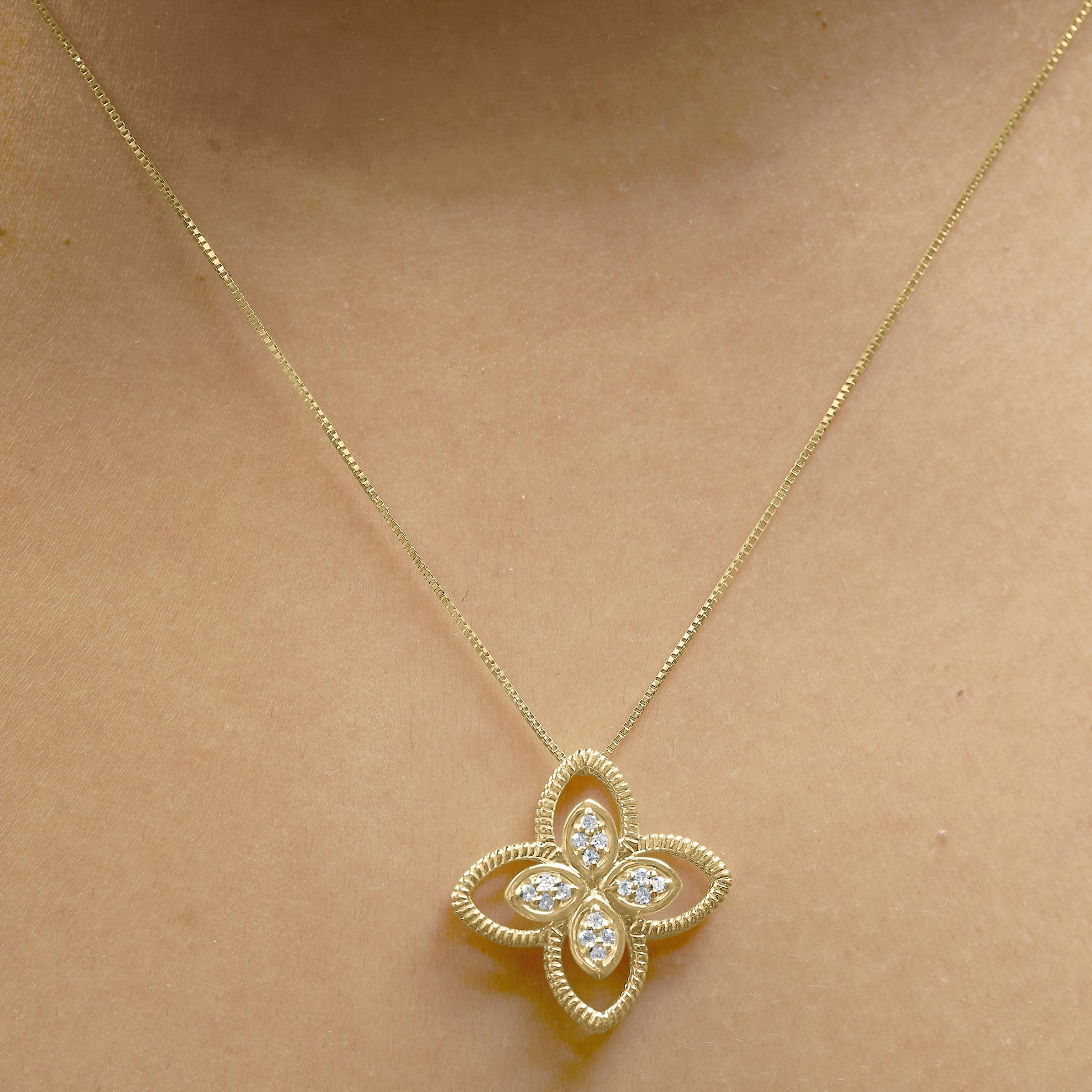 Yellow metal necklace with a flower-shaped pendant featuring white round gemstones in prong settings, worn on a model, front-facing angle.