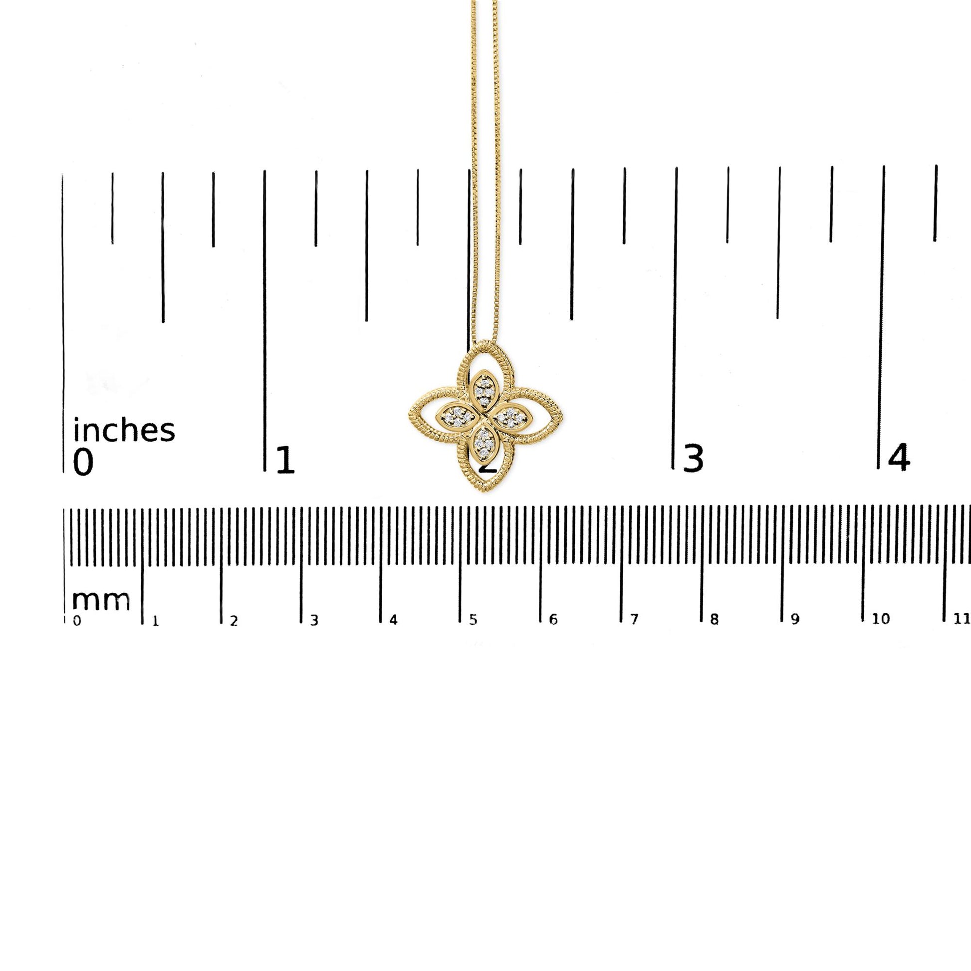 Yellow metal necklace with a flower-shaped pendant featuring white round gemstones in prong settings, shown from the front on a ruler for size reference.