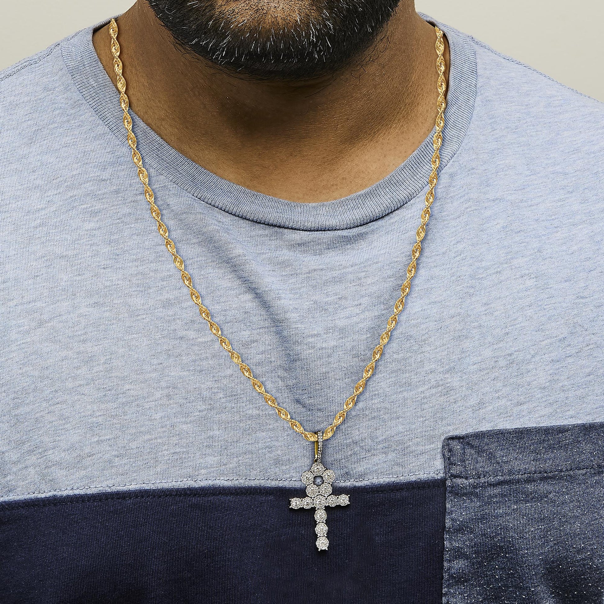 Close-up front view of a model wearing a yellow metal twisted rope necklace with a cross-shaped pendant adorned with white gemstones in prong settings.