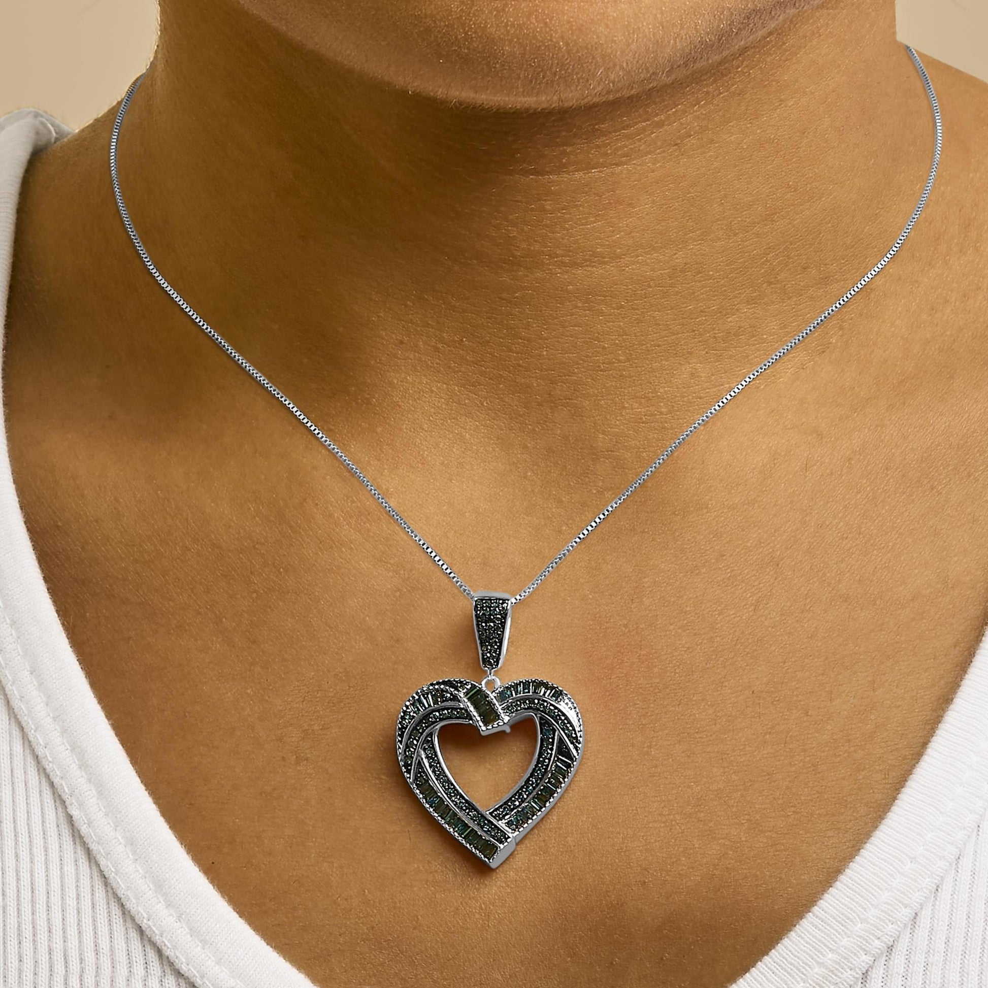 Necklace with a heart-shaped pendant featuring blue round prong and baguette channel-set gemstones on a white metal chain, shown worn on a model in a close-up frontal shot.