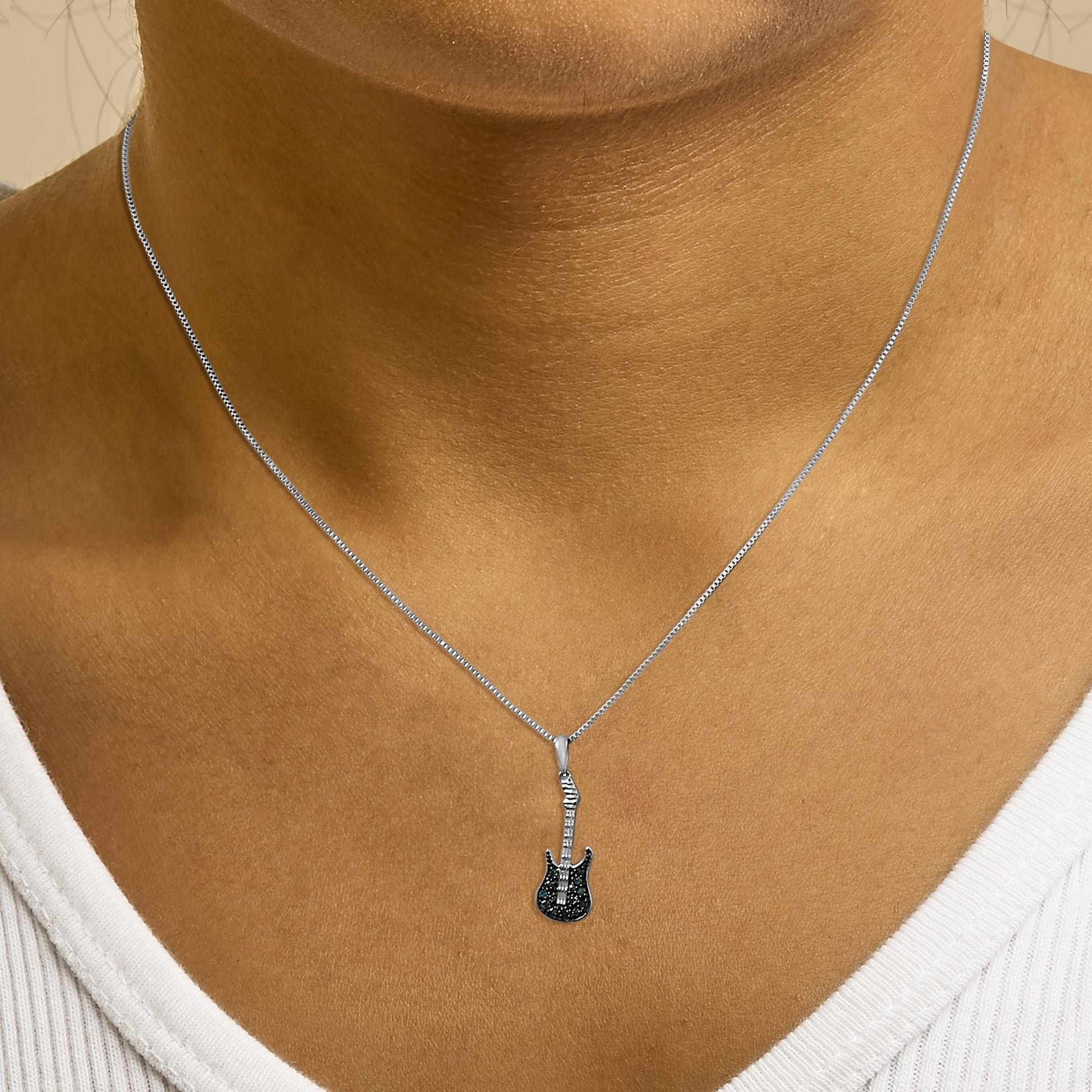 Close-up front view of a white metal necklace on a model featuring a guitar-shaped pendant with blue round gemstones in prong settings.