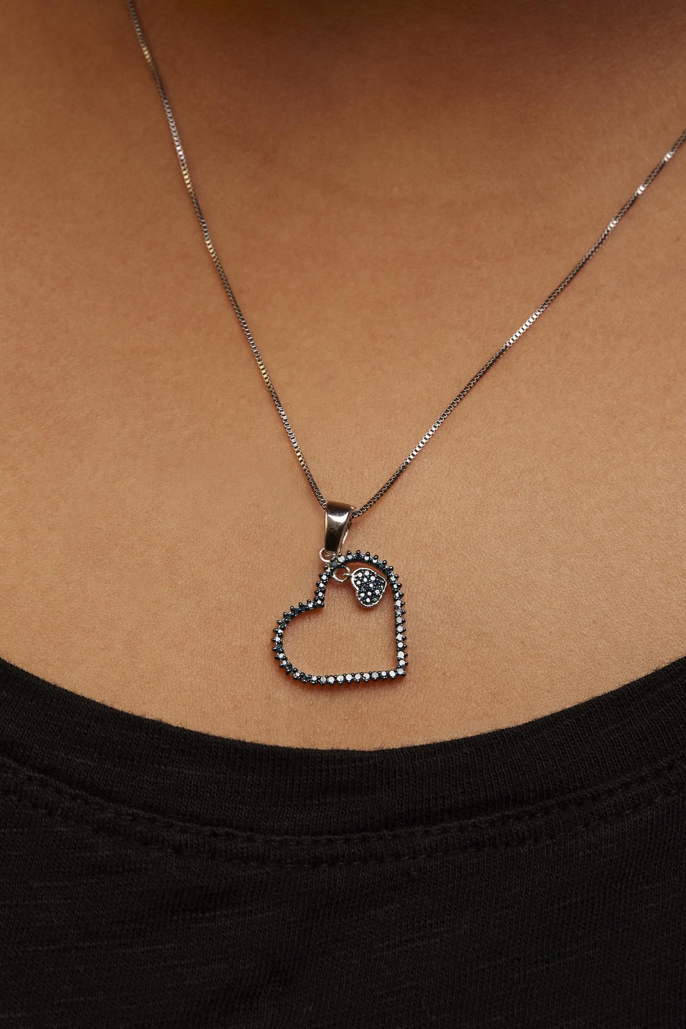 Close-up front view of a model wearing a white metal necklace with a heart-shaped pendant adorned with round prong-set blue gemstones.