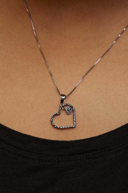 Close-up front view of a model wearing a white metal necklace with a heart-shaped pendant adorned with round prong-set blue gemstones.