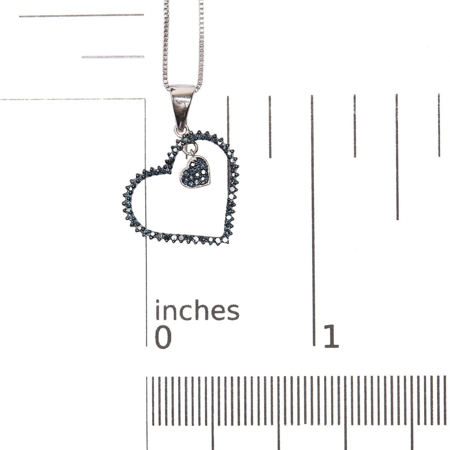 Close-up front view of a white metal heart-shaped necklace pendant with two open heart outlines, each adorned with prong-set blue round gemstones, shown on a scale.