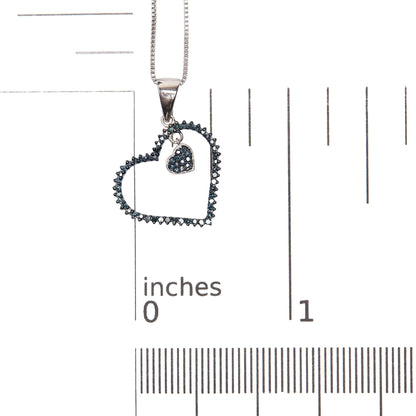 Close-up front view of a white metal heart-shaped necklace pendant with two open heart outlines, each adorned with prong-set blue round gemstones, shown on a scale.