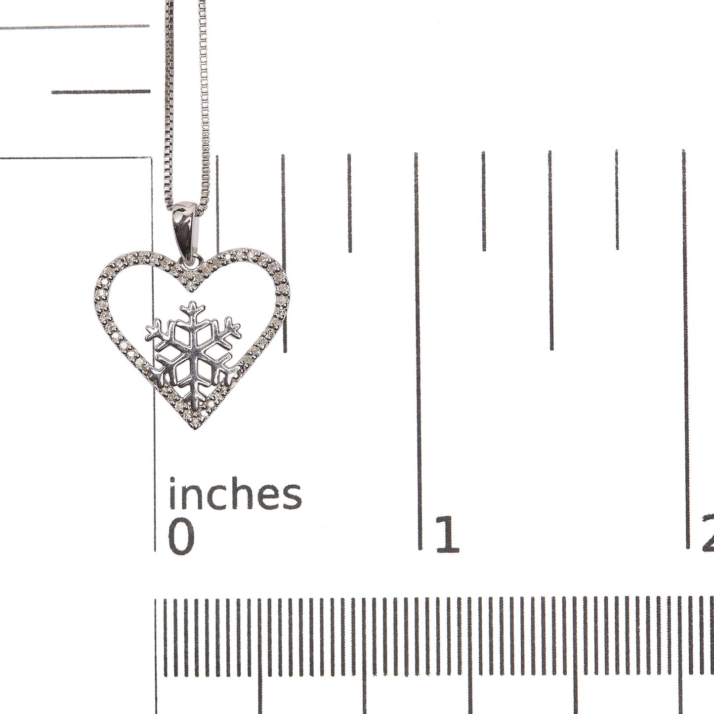 Close-up image of a white necklace pendant with a heart shape adorned with white gemstones set in prongs along the edge and a snowflake design inside, shown on a scale.