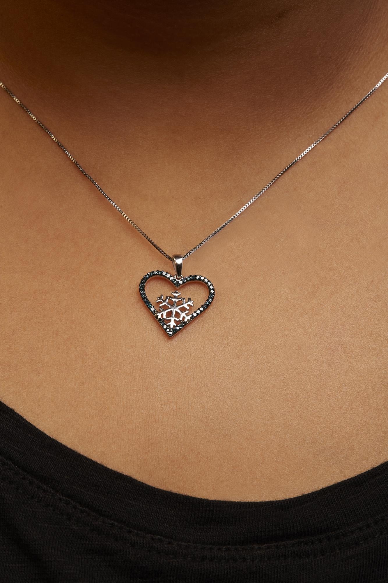 White necklace with a heart-shaped pendant featuring a snowflake design inside, outlined with round blue gemstones in prong settings, shown worn on a model from a close-up front angle.