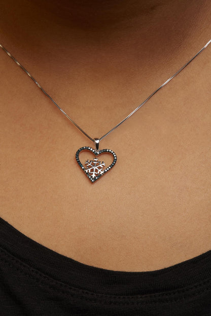 White necklace with a heart-shaped pendant featuring a snowflake design inside, outlined with round blue gemstones in prong settings, shown worn on a model from a close-up front angle.