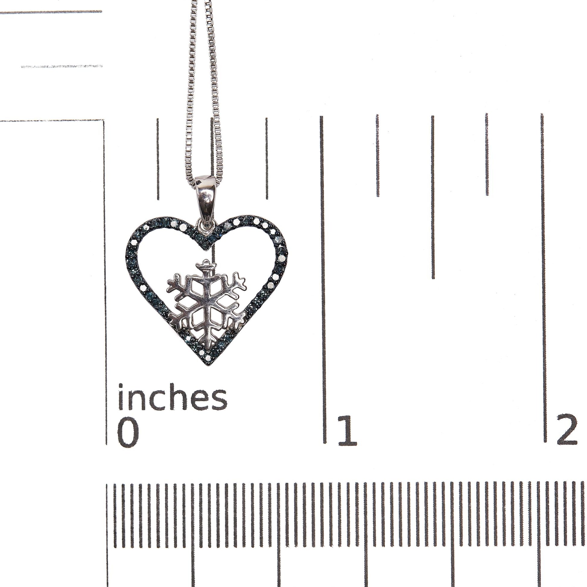 Close-up front view of a white metal heart-shaped necklace pendant with a snowflake design inside, outlined with round prong-set blue gemstones, shown on a scale.