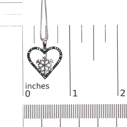 Close-up front view of a white metal heart-shaped necklace pendant with a snowflake design inside, outlined with round prong-set blue gemstones, shown on a scale.