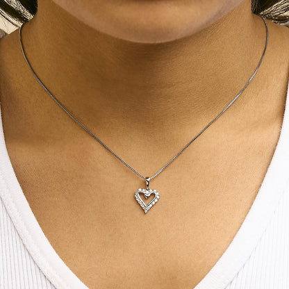 Close-up front view of a white metal heart-shaped pendant necklace with round white gemstones in prong settings, worn on a model.