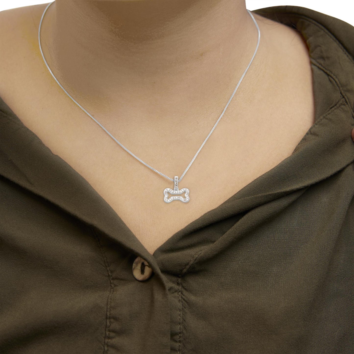 Close-up front view of a white metal necklace on a model, featuring a bone-shaped pendant adorned with round white gemstones in prong settings.