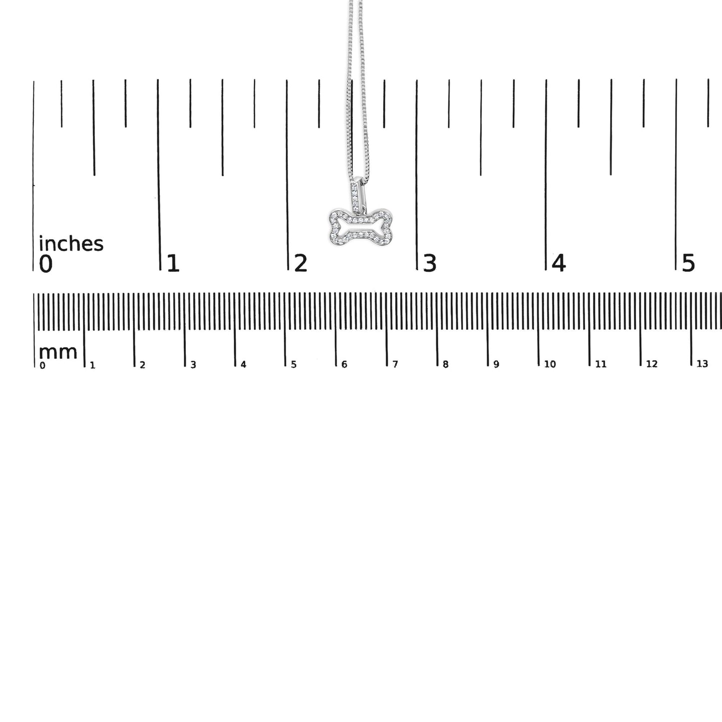 Close-up front view of a white metal bone-shaped pendant necklace with round white gemstones in prong settings, shown on a ruler for size reference.