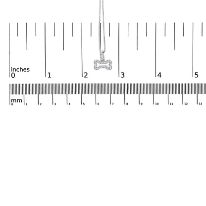 Close-up front view of a white metal bone-shaped pendant necklace with round white gemstones in prong settings, shown on a ruler for size reference.