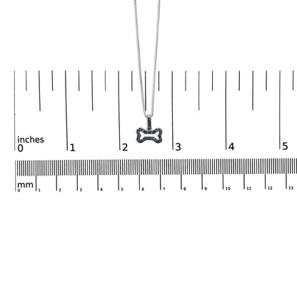 White metal necklace with bone-shaped pendant set with round blue gemstones in prong settings, shown hanging centered above a ruler for size reference, front view.