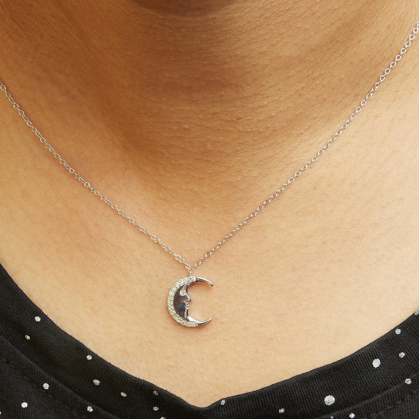 White metal necklace with crescent moon pendant featuring round white gemstones in prong settings, shown on a model from a front angle.