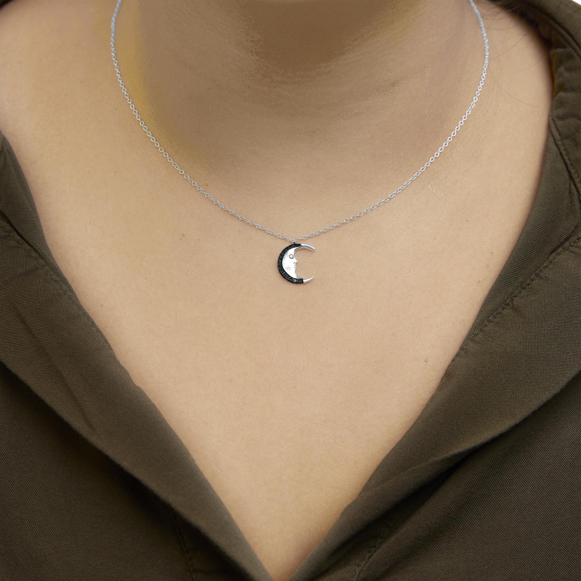 Close-up front view of a white metal necklace on a model with a crescent moon pendant adorned with round blue gemstones in a prong setting.