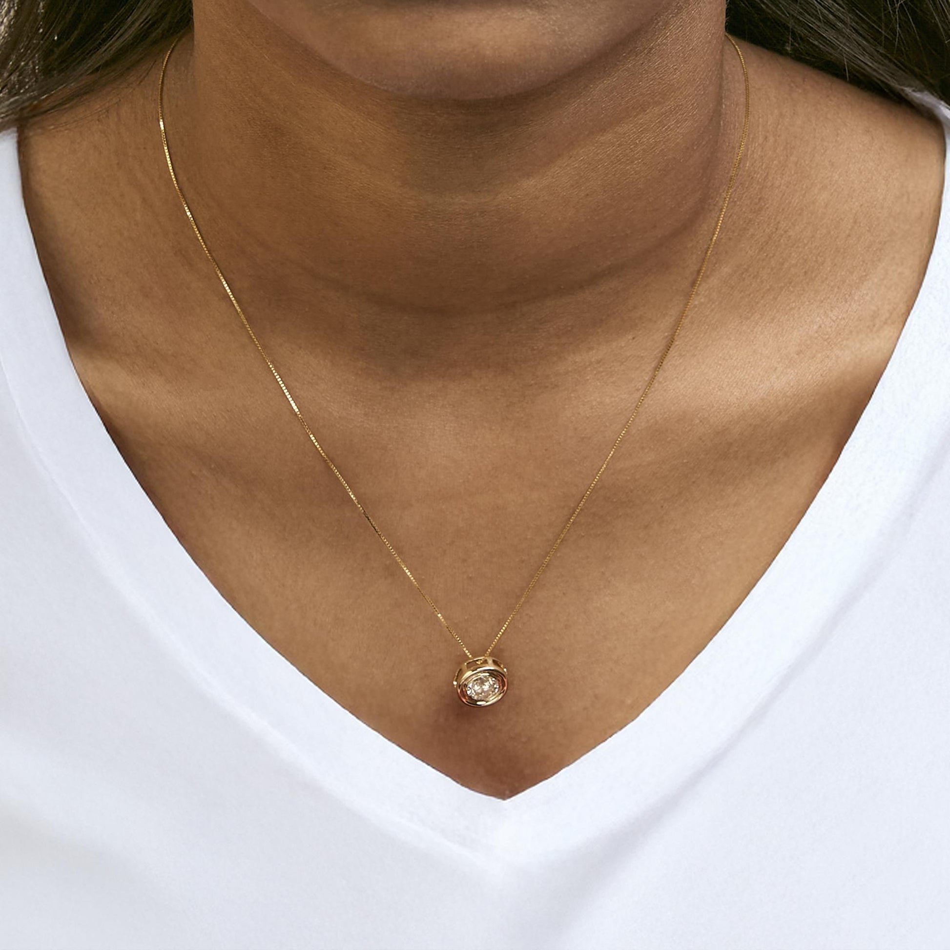 Close-up front view of a model wearing a yellow metal necklace with a round bezel-set white gemstone pendant.