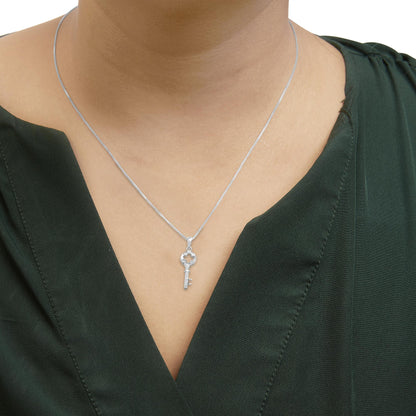Close-up front view of a white metal necklace with a key-shaped pendant adorned with round white gemstones, worn on a model with a green top.