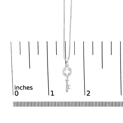White metal key-shaped necklace pendant with round white gemstones in prong settings, shown hanging on a chain against a ruler for size reference, front-facing angle.