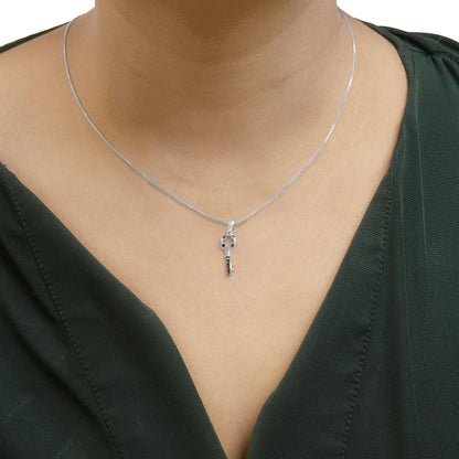 Close-up front view of a white metal necklace with a key-shaped pendant featuring round blue gemstones in prong settings, worn on a model.