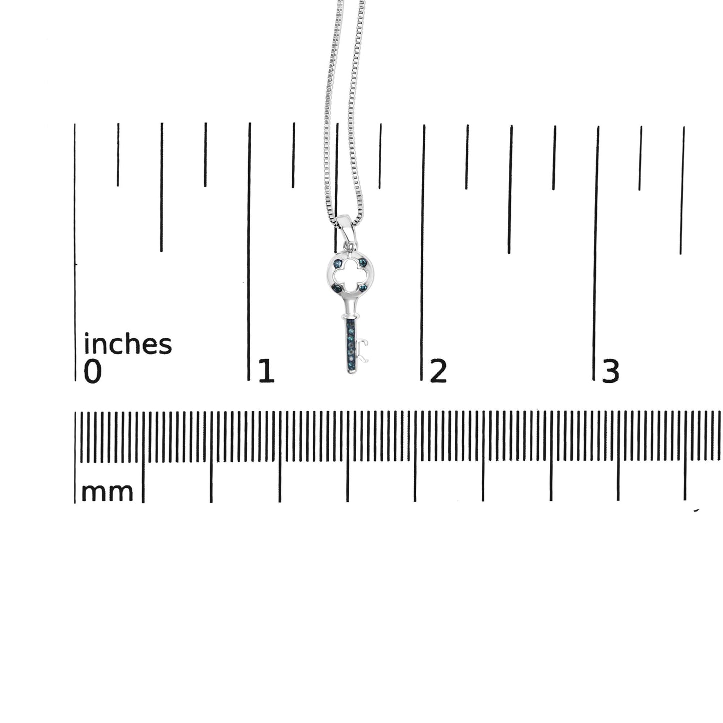 Close-up front view of a white metal key-shaped necklace pendant with round blue gemstones in prong settings, shown on a ruler for size reference.