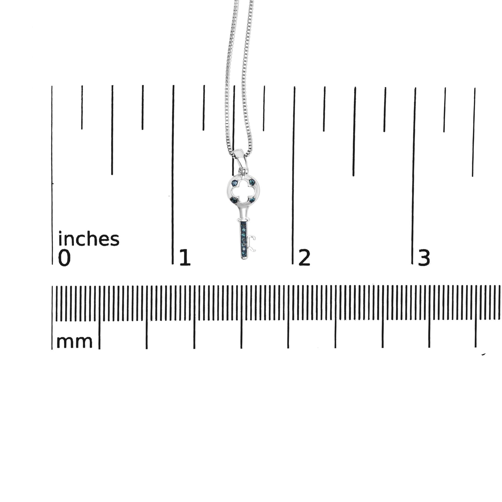 Close-up front view of a white metal key-shaped necklace pendant with round blue gemstones in prong settings, shown on a ruler for size reference.