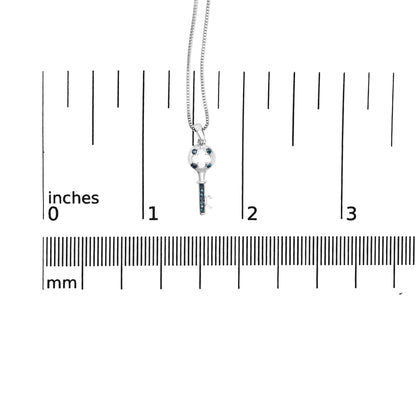Close-up front view of a white metal key-shaped necklace pendant with round blue gemstones in prong settings, shown on a ruler for size reference.