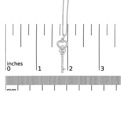 Front view of a white metal key-shaped necklace pendant with round white gemstones, displayed on a ruler for size reference.