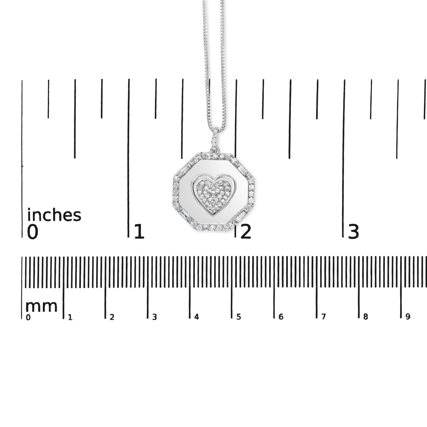 Front view of a white necklace pendant with an octagonal frame set with round and baguette white gemstones surrounding a heart shape filled with round white gemstones, displayed on a ruler for size reference.