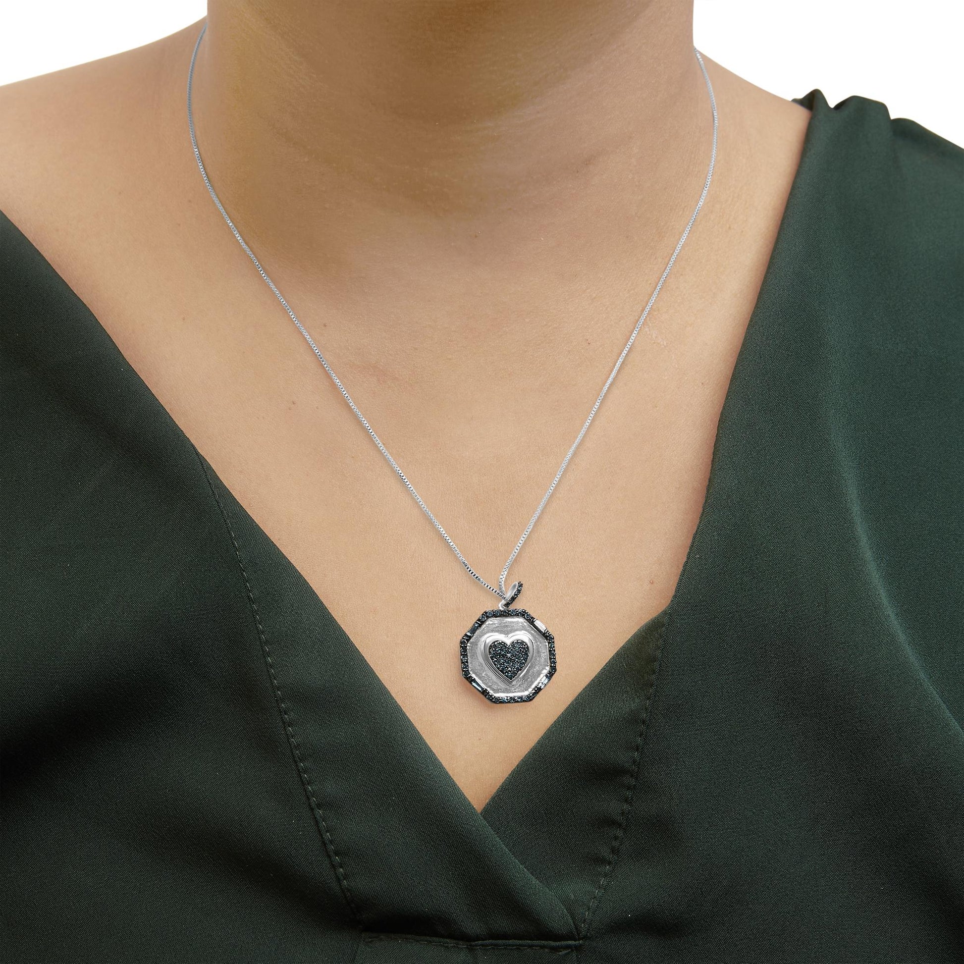 Close-up front view of a white metal necklace with an octagonal pendant featuring a heart shape in the center, both accented with blue round and baguette gemstones, worn on a model.