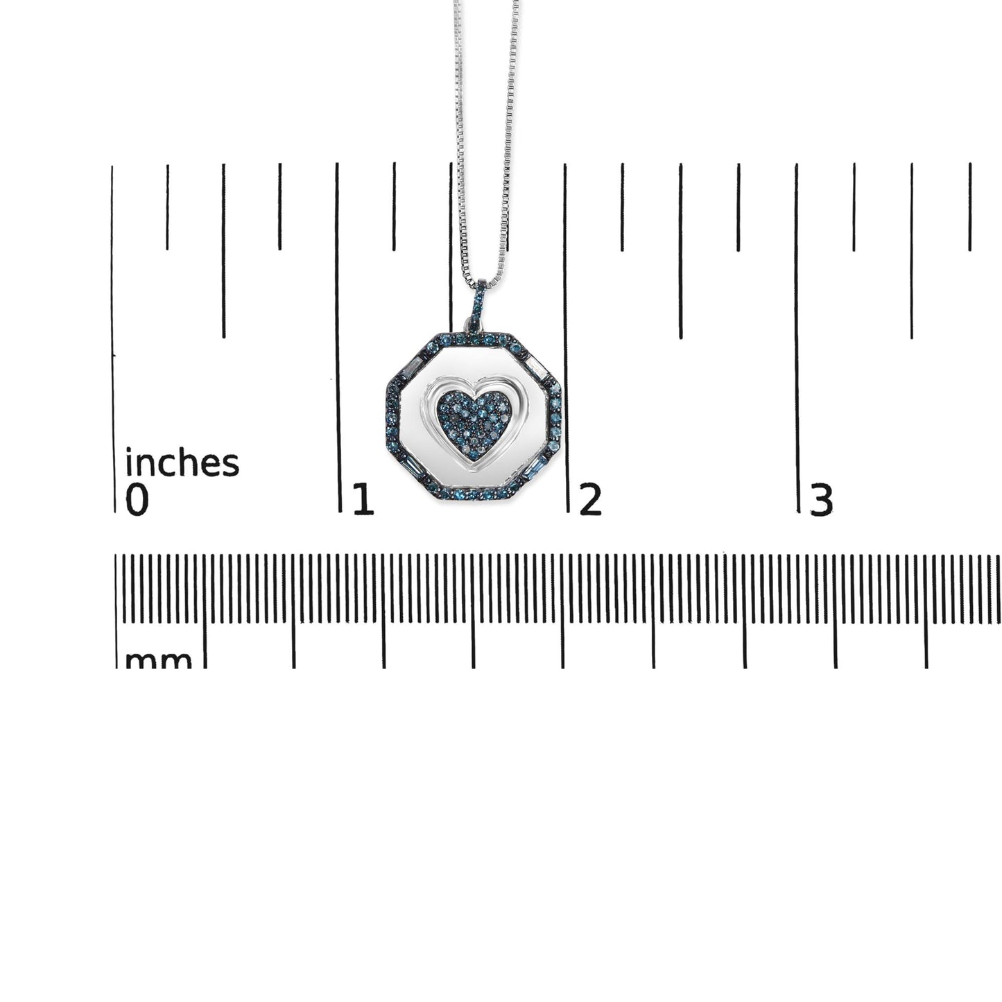 Close-up front view of a white necklace pendant with a heart shape in the center, surrounded by an octagonal frame set with small blue round and baguette-shaped gemstones, displayed on a ruler for size reference.