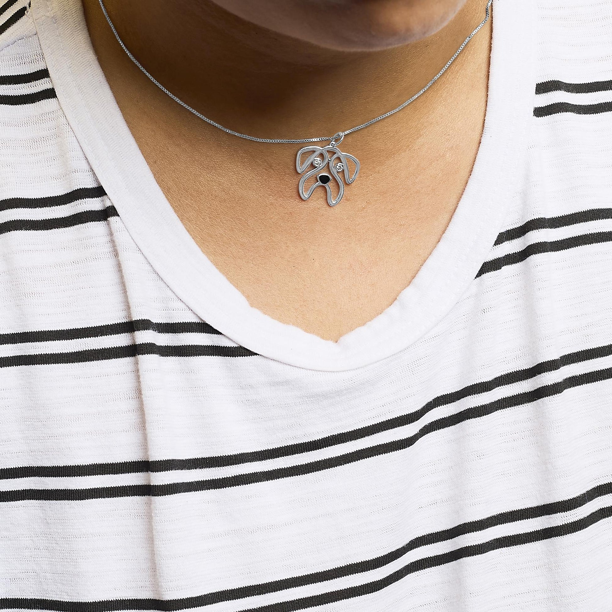 White metal necklace with an abstract dog face pendant featuring two round white gemstones in bezel settings, shown from a front view on a model wearing a white and black striped shirt.