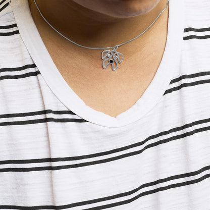 White metal necklace with an abstract dog face pendant featuring two round white gemstones in bezel settings, shown from a front view on a model wearing a white and black striped shirt.