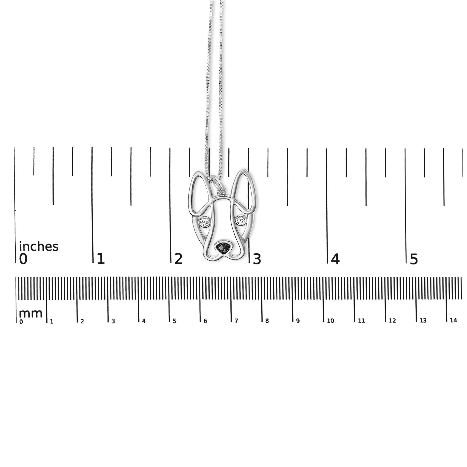 White metal necklace with a dog face pendant featuring two round bezel-set white gemstones for eyes, shown hanging centered over a ruler for size reference, photographed from the front.