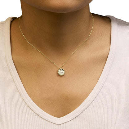 Yellow metal necklace with a round pendant featuring multiple white round gemstones set in prongs, shown worn on a model from a front angle.