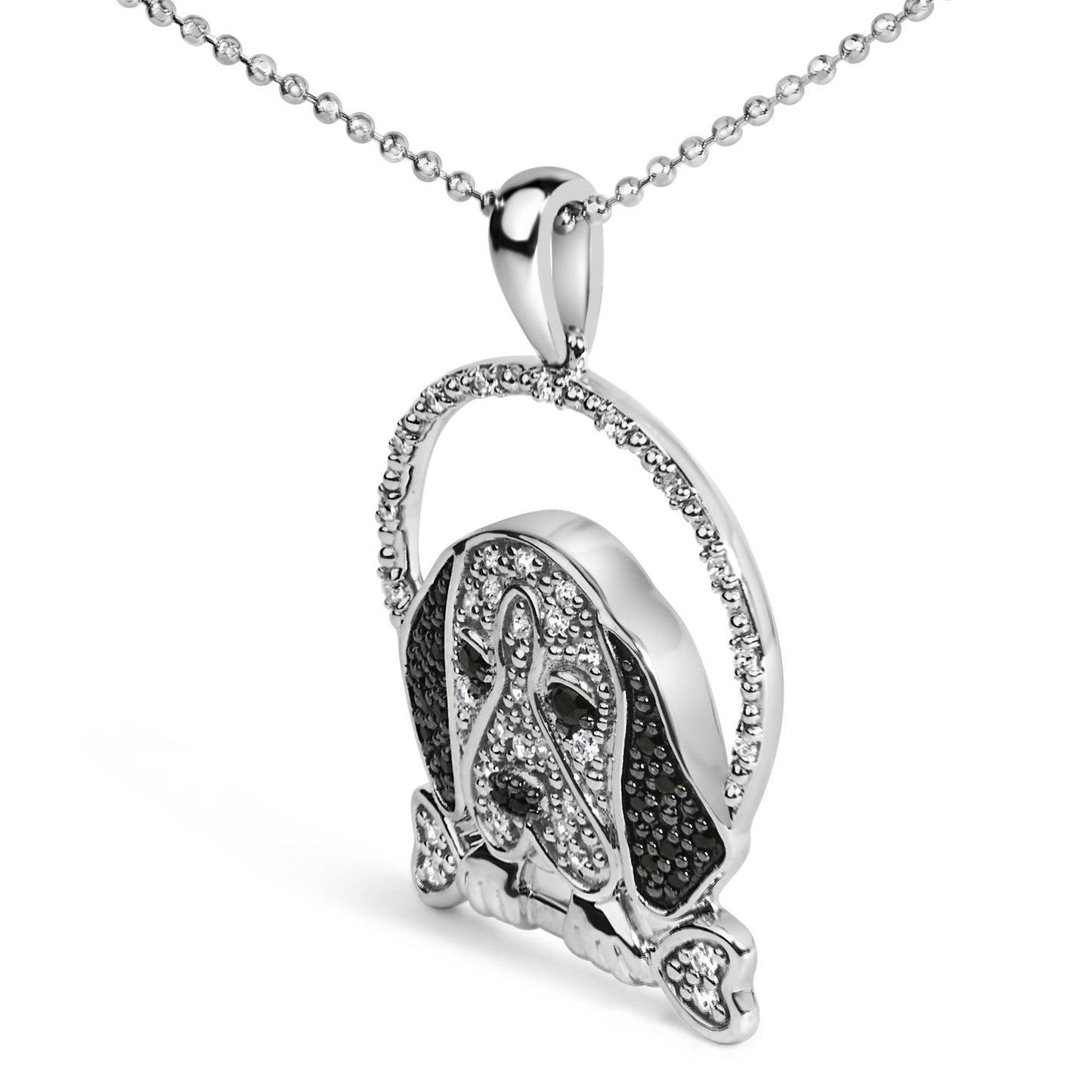 Close-up angled view of a white metal necklace pendant shaped like a dog's face holding a bone in its mouth, decorated with white and black round micro-pave and prong-set gemstones.