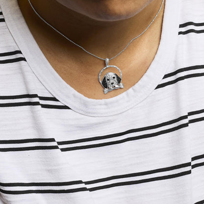 Close-up front view of a white metal necklace on a model featuring a dog-shaped pendant decorated with white and black gemstones in various settings, holding a bone in its mouth.
