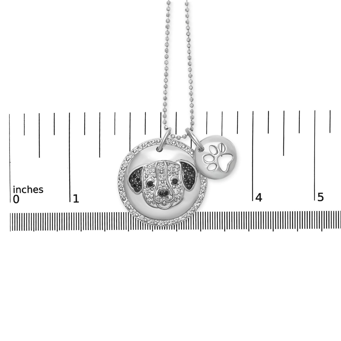 White metal necklace with two round pendants, one featuring a dog face adorned with white and black gemstones, and the other a paw print cutout, shown on a ruler for size reference, front-facing angle.