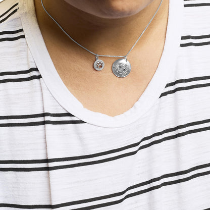 Close-up front view of a white metal necklace with two round pendants on a model, featuring small white and black gemstones in various settings.