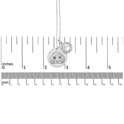 White metal necklace with two round pendants, one featuring a dog face design with white and black gemstones, and the other a paw print surrounded by white gemstones, photographed from the front on a ruler for size reference.