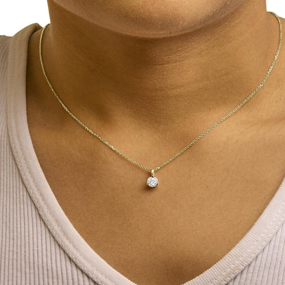 Close-up front view of a yellow metal necklace with a single round white gemstone in a three-prong setting, worn on a model.