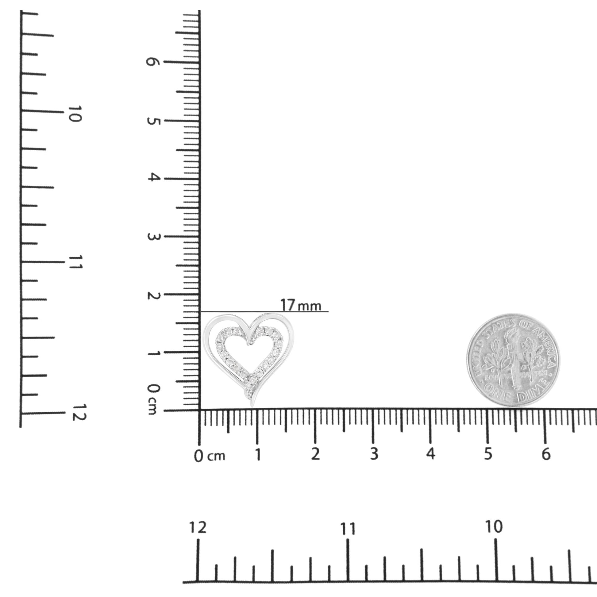 Close-up front view of a white metal heart-shaped necklace pendant with prong-set round white gemstones, shown on a ruler and next to a dime for size reference.