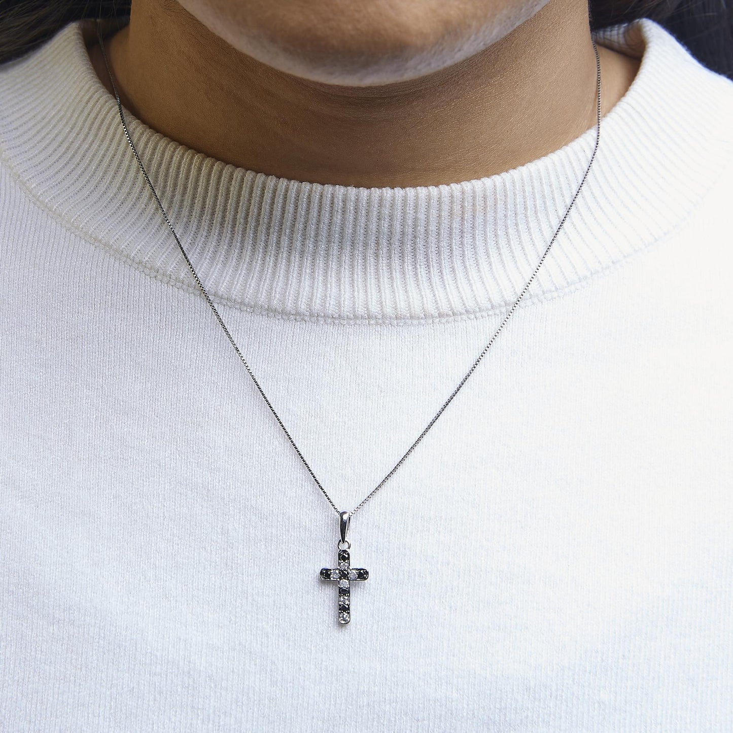 Necklace with a white metal cross pendant featuring alternating black and white round prong-set gemstones, worn on a model, front-facing angle.